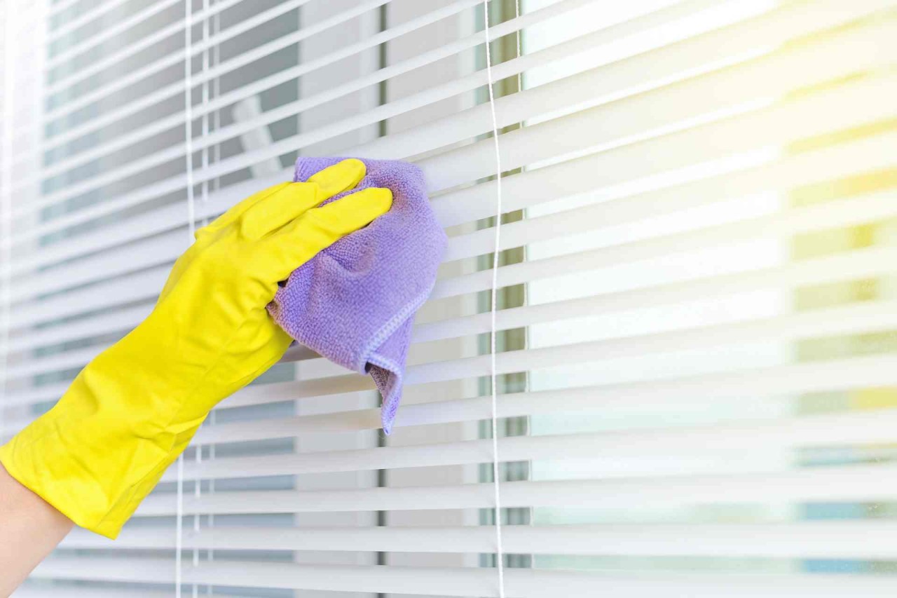 A person wearing a yellow glove and cleaning mini blinds with a purple microfiber rag at Blind King near Providence, RI